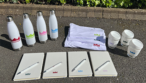 Company Rebranding with multiple colour logos on bottles, notebooks, pens, coffee cups, and t-shirts